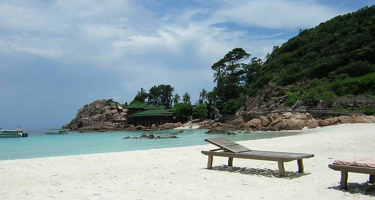 Tropischer Strand mit türkisfarbenem Wasser und Liegestühlen.