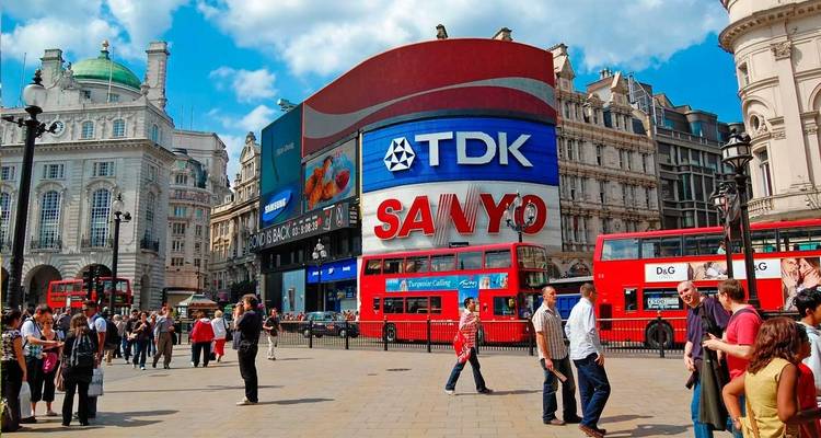 Piccadilly Circus bondé de monde, avec ses bus rouges emblématiques et ses panneaux publicitaires électroniques colorés.