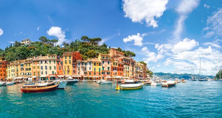 Port animé de Portofino avec des bâtiments colorés, des bateaux et une eau émeraude sous un ciel bleu éclatant.