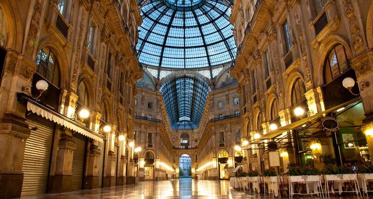 Intérieur élégant de la Galleria Vittorio Emanuele II à Milan avec dôme de verre et devantures de magasins illuminées.
