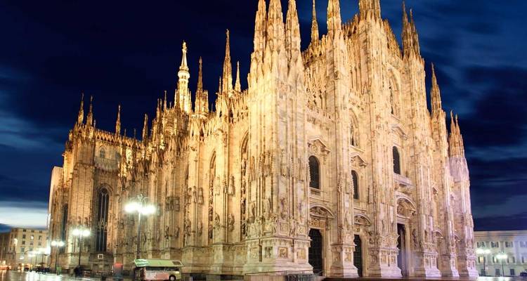 Les flèches gothiques du Duomo illuminé de Milan s'élevant de façon spectaculaire contre un ciel nocturne bleu profond.
