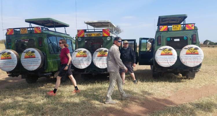 Tourists standing by safari vans in the grassland.