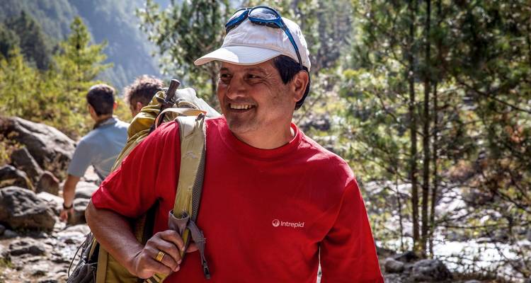 Vriendelijke trektocht gids met rugzak die glimlacht langs een bosrijk Himalaya-pad