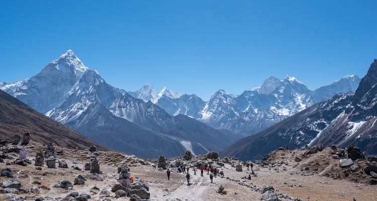 Fila de trekistas atravesando un valle himalayo de altura rodeado de picos imponentes