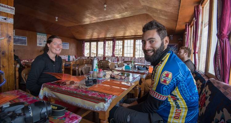 Los compañeros de trekking se relajan dentro de una casa de té nepalí, sonriendo alrededor de mesas de madera.