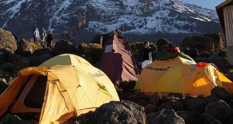 Des tentes avec des personnes installées au pied d'une montagne enneigée.