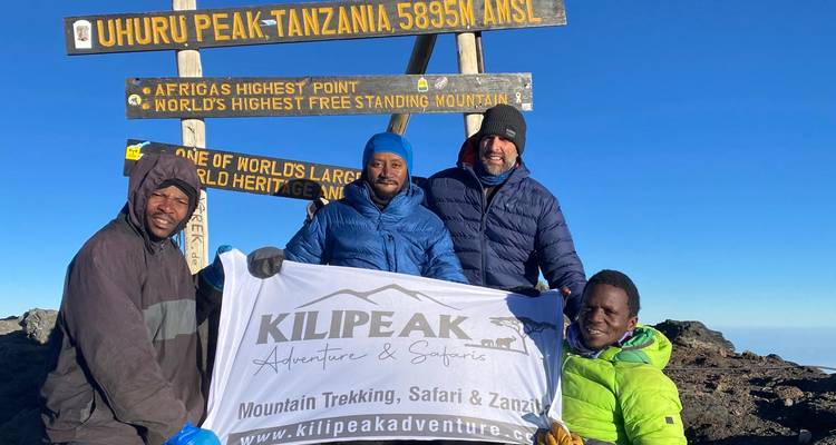 Group of hikers posing at Uhuru Peak on Mount Kilimanjaro with elevation signs.