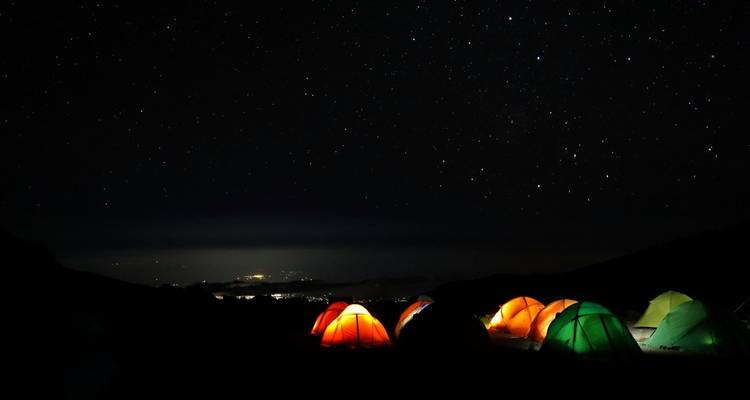 Scène de camping nocturne avec des tentes éclairées sous un ciel étoilé.