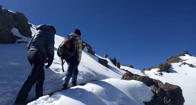 Deux randonneurs gravissant une pente de montagne enneigée.