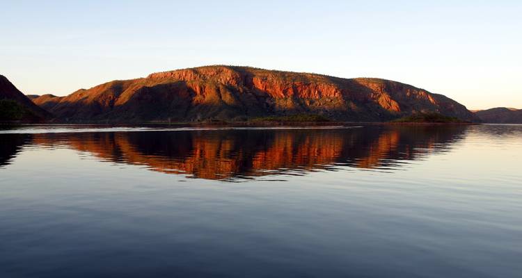 Mountain landscape reflected in calm water at sunset.