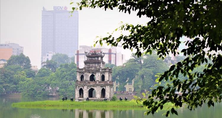 Torre de piedra rodeada de vegetación en un entorno de lago urbano.