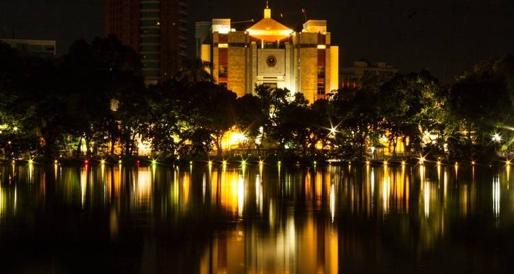 Edificio iluminado con luces reflejadas en un lago por la noche.
