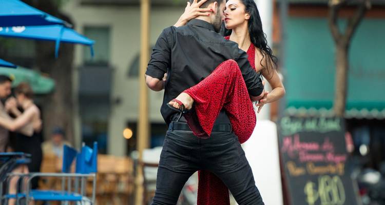 Pareja bailando tango en una calle de la ciudad con gente de fondo.
