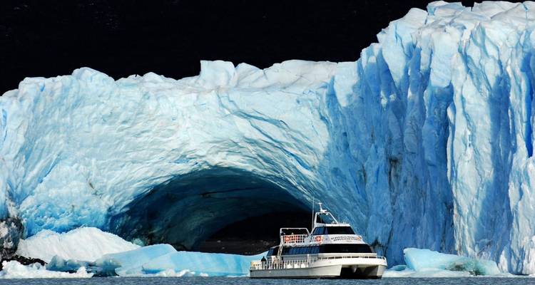 Barco acercándose a un gran glaciar con una cueva azul profunda.