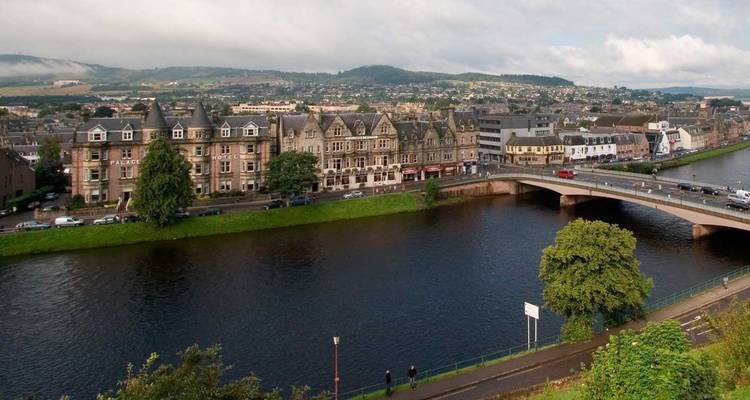 River Ness flowing through Inverness with stone terraced buildings and a bridge connecting the banks under patchy clouds