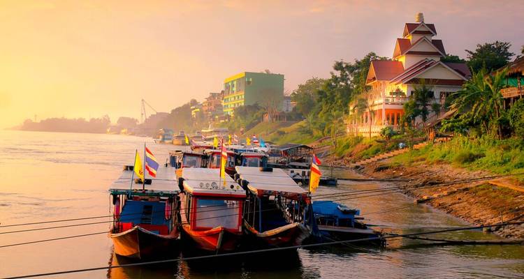 Colorful boats docked on a river at sunset with nearby buildings.