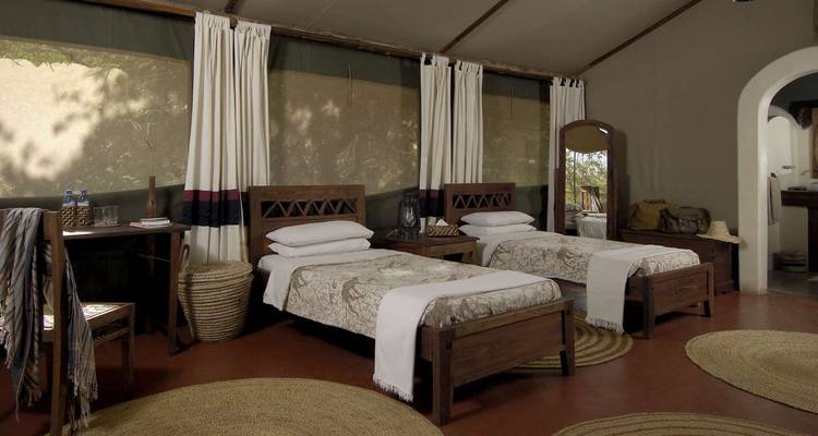 Eenvoudige safari lodge kamer met twee aparte bedden en aardse tinten.