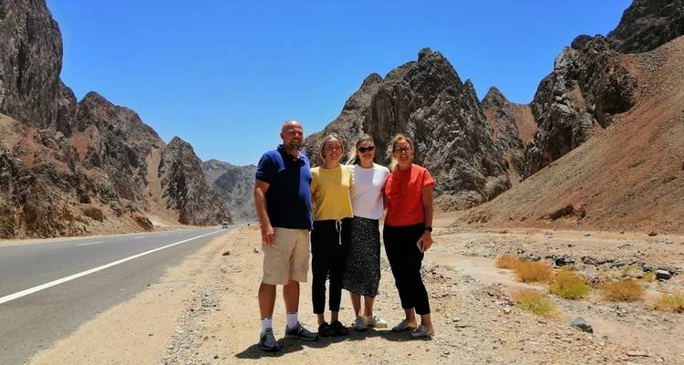 A group of four people standing on a road in a mountainous area.