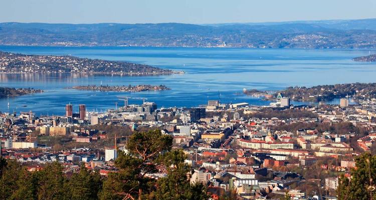 Uitgestrekt uitzicht over Oslo en zijn fjord met verspreide eilanden en blauw water omlijst door beboste heuvels.