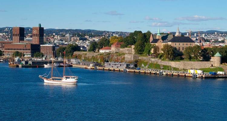 Uitzicht over de haven van Oslo met het Akershus-fort en de bakstenen torens van het stadhuis van Oslo onder een blauwe hemel.