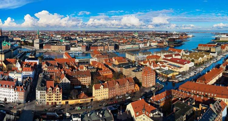 Vista panorámica aérea del paisaje urbano de Copenhague con techos rojos atravesado por canales y el mar distante.