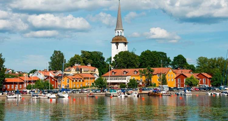 Village portuaire pittoresque aux maisons colorées et au clocher d'église se reflétant dans l'eau calme.