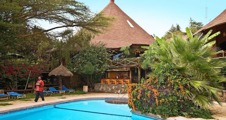 A resort with a swimming pool, lush greenery, and a person walking nearby.