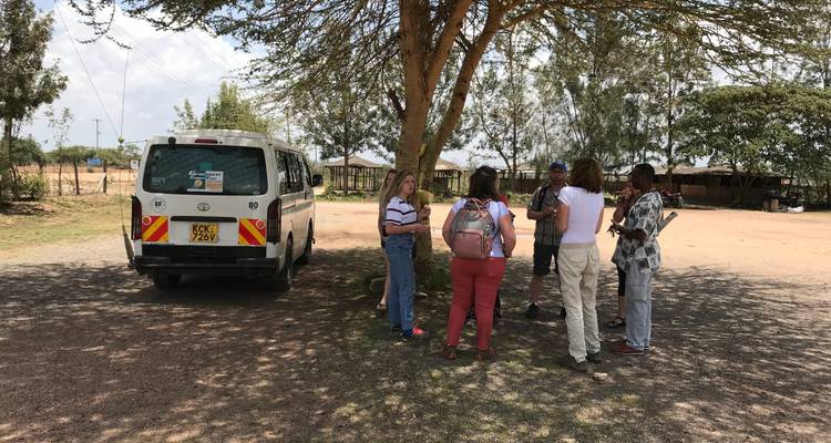 A group of people and a van parked under a tree in a rural area.