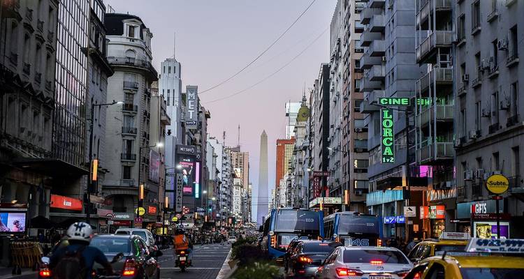 El movido tráfico de la Avenida Corrientes enmarca el Obelisco a lo lejos entre los rascacielos de Buenos Aires al atardecer