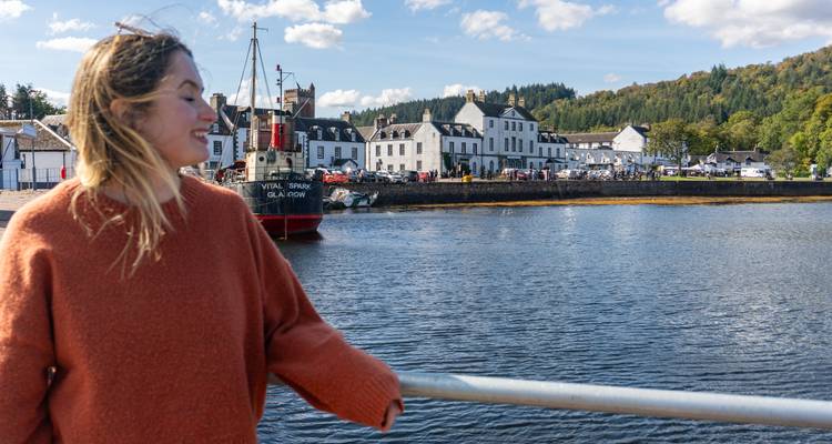 Femme heureuse en pull rouge debout près d'un front de mer avec un bateau et des bâtiments.