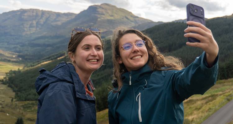 Deux amis prenant un selfie avec un paysage montagneux pittoresque en arrière-plan.