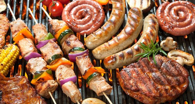Assortiment de viandes grillées et de légumes sur un barbecue.