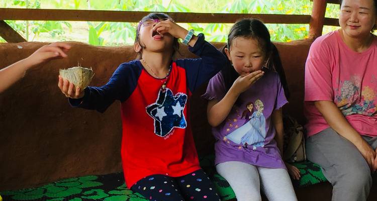 Des enfants goûtent des morceaux de noix de coco fraîche assis sur un banc rustique, sous la supervision d'un adulte.