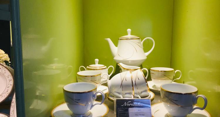 Vitrine éclairée en vert présentant un service à thé Noritake blanc et doré avec tasses et soucoupes.