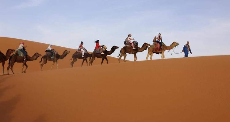 Camels and riders trekking over sand dunes.