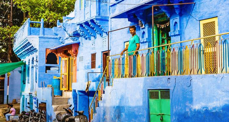 Homme debout sur un balcon de maisons peintes en bleu.