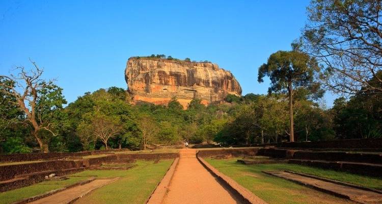 Sentier menant à la formation rocheuse emblématique de Sigiriya sous un ciel bleu dégagé.