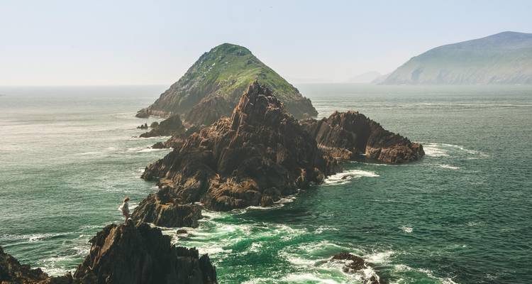 Een ruige rotsachtige schiereiland steekt uit in de Atlantische Oceaan met schuimende turquoise golven eronder.
