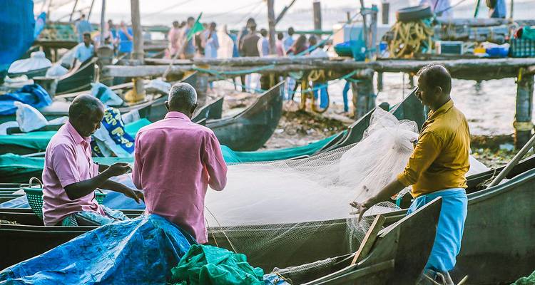 Des pêcheurs s'occupant de leurs filets à côté de leurs bateaux avec un port animé en arrière-plan.
