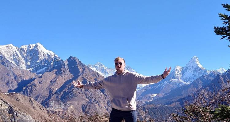 Homme debout les bras étendus entouré de montagnes.