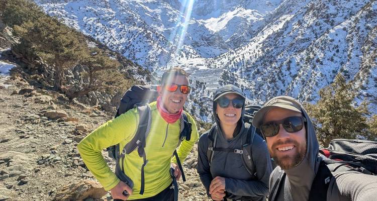 Trois randonneurs posant avec des montagnes enneigées en arrière-plan.