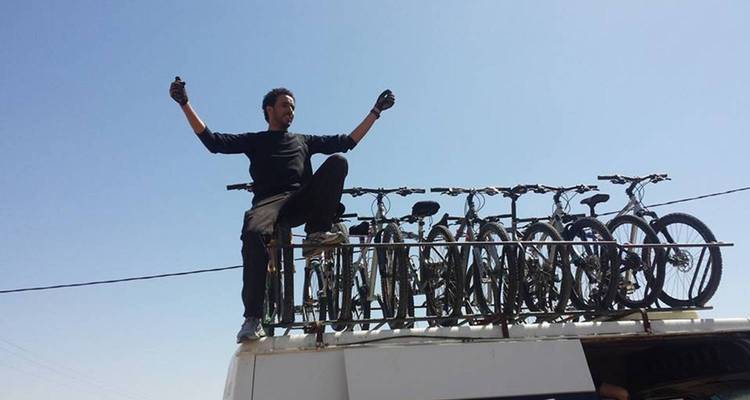 Personne triomphant debout sur le toit d'un véhicule avec des bicyclettes en arrière-plan.