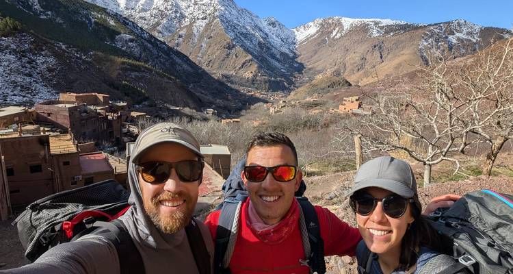 Trois personnes souriantes avec une vallée et des sommets enneigés au loin.