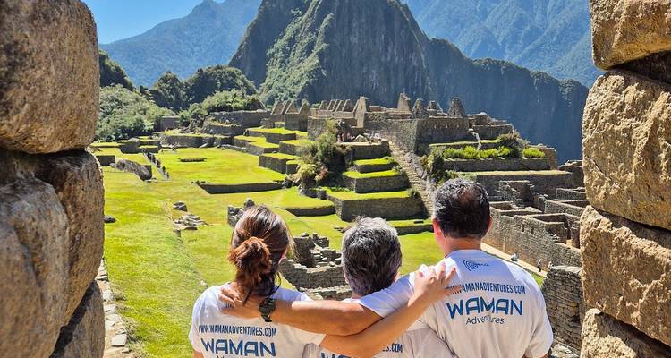 Tres personas contemplando Machu Picchu con montañas en la distancia.