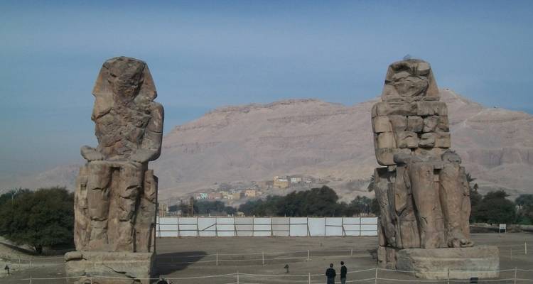 Twee kolossale stenen figuren gezeten in een kaal landschap.