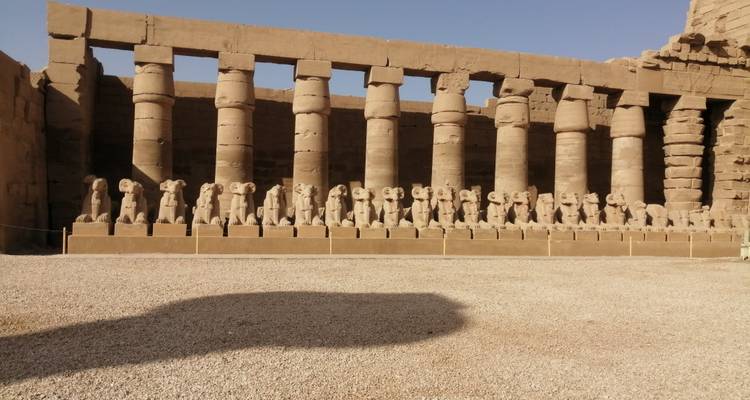 Rij van beelden langs een pad dat leidt naar grote zuilen op een antieke locatie.