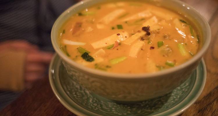 Gros plan d'une soupe thaïlandaise crémeuse garnie d'herbes dans un bol décoratif sur une table en bois.