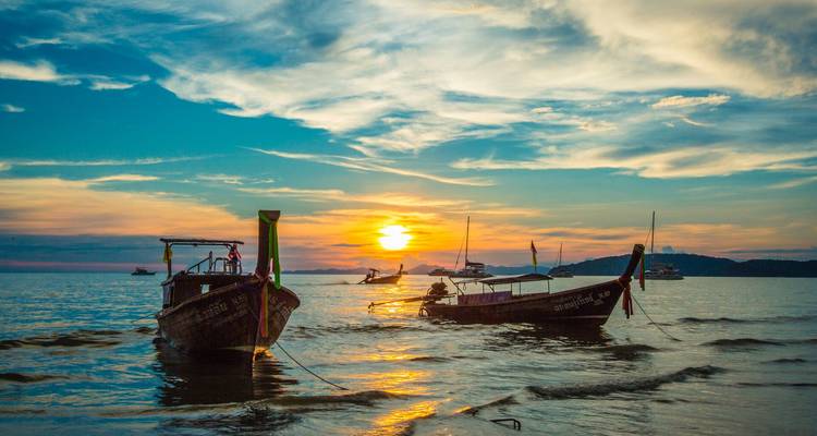 Les bateaux à longue queue ancrés dans les eaux peu profondes lors d'un coucher de soleil vibrant avec une mer calme et les silhouettes lointaines des îles.