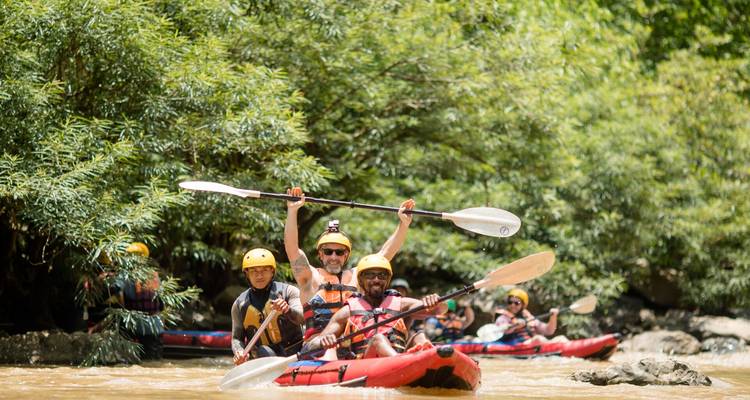 Les voyageurs casqués pagaient des kayaks gonflables rouges dans une rivière de la jungle, levant les pagaies en signe de célébration.
