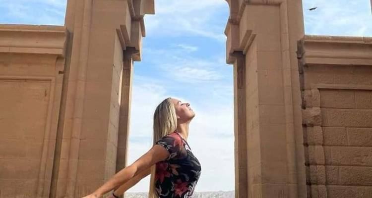 Persoon die poseert met uitgestrekte armen te midden van oude Egyptische ruïnes.